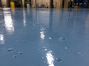 Why Epoxy Floors Bubble and How Contractors Can Prevent It 7 Raised air bubbles scattered across a glossy blue epoxy floor in an industrial facility.