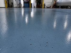 Why Epoxy Floors Bubble and How Contractors Can Prevent It 8 Numerous small pinholes visible across the surface of a blue industrial epoxy floor.